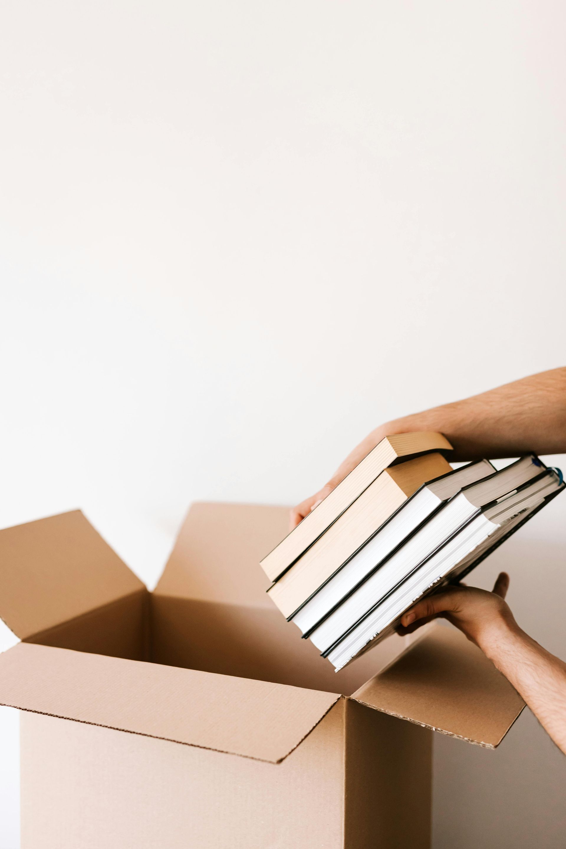 A person is putting a stack of books into a cardboard box.