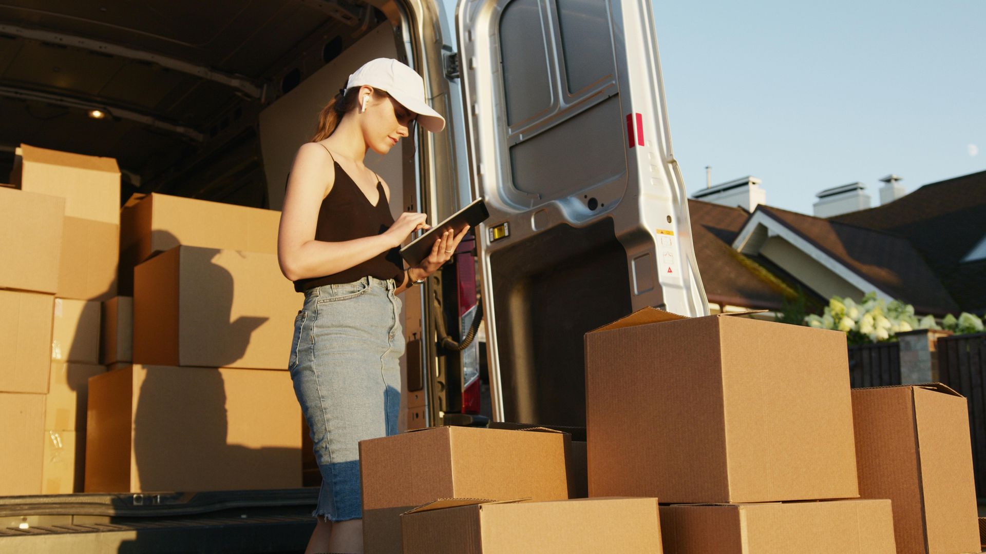 A woman is standing in front of a van filled with cardboard boxes.