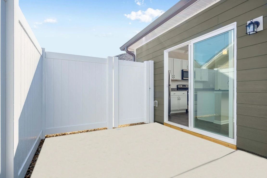 A patio with a white fence and sliding glass doors leading to a kitchen.