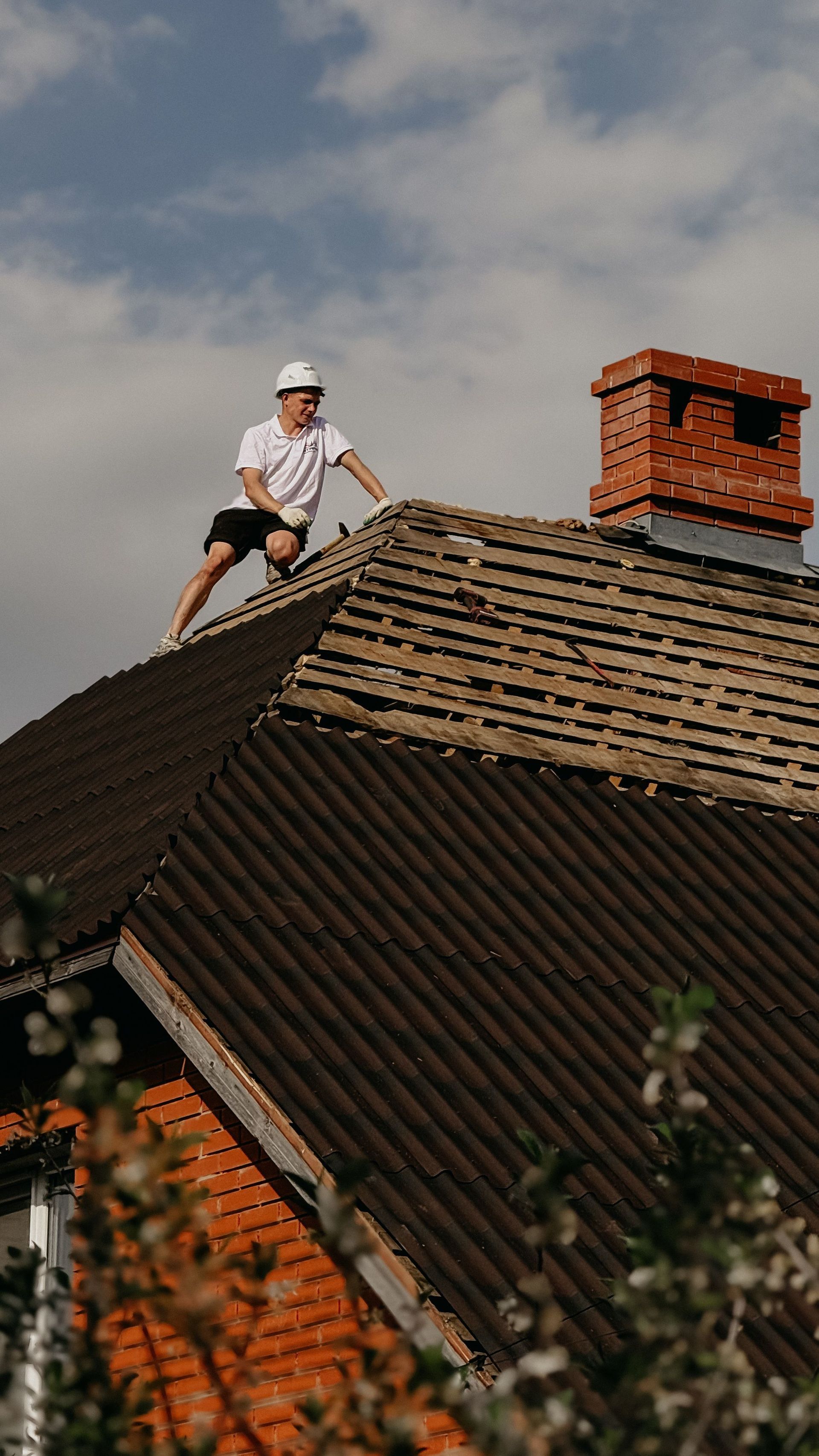 Worker on a tiled rooftop beside a brick chimney, wearing a white helmet and clothes.