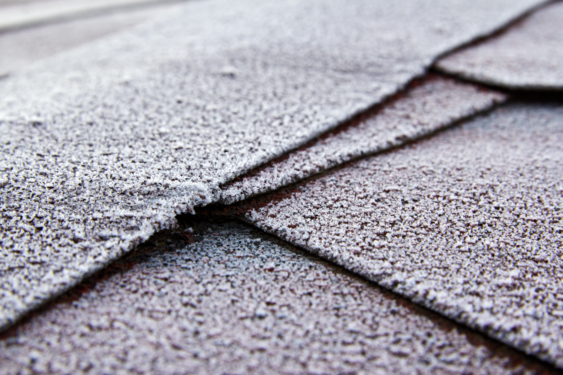 Close-up of overlapping gray roof shingles with rough, textured surfaces.