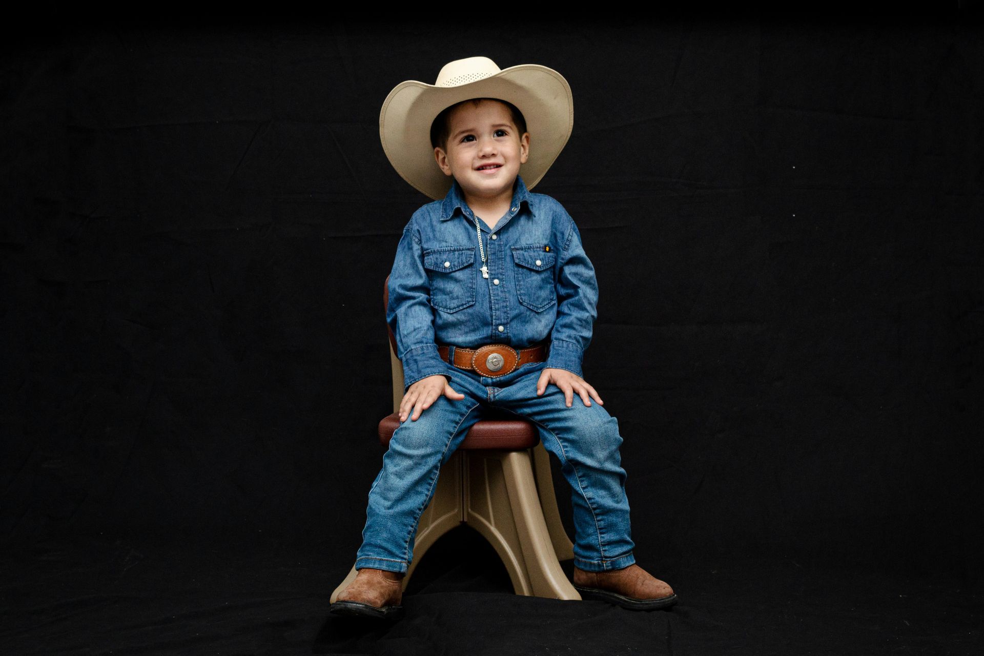 A young boy in a cowboy hat is sitting on a chair.