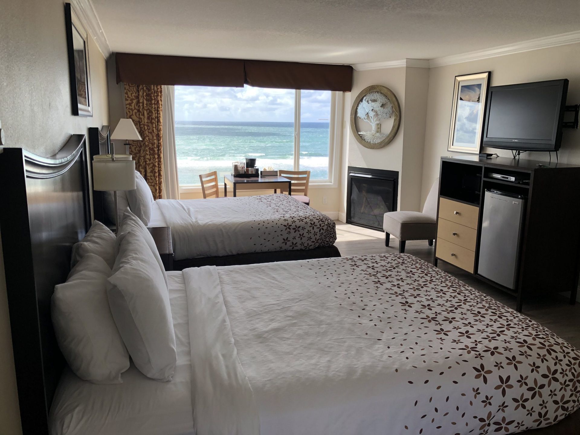 Hotel room with two beds, ocean view, television, small desk, and a refrigerator.