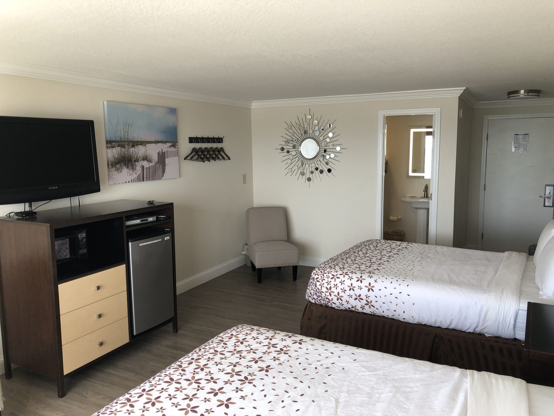Hotel room with two beds, TV, dresser, mini-fridge, chair, and bathroom.
