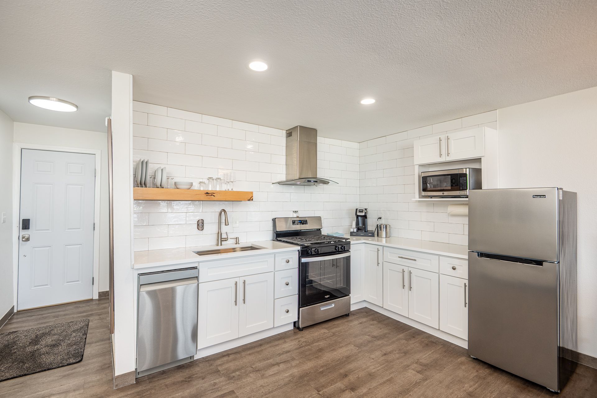 A modern kitchen with white cabinets, stainless steel appliances, white subway tile backsplash, and wood-look flooring.