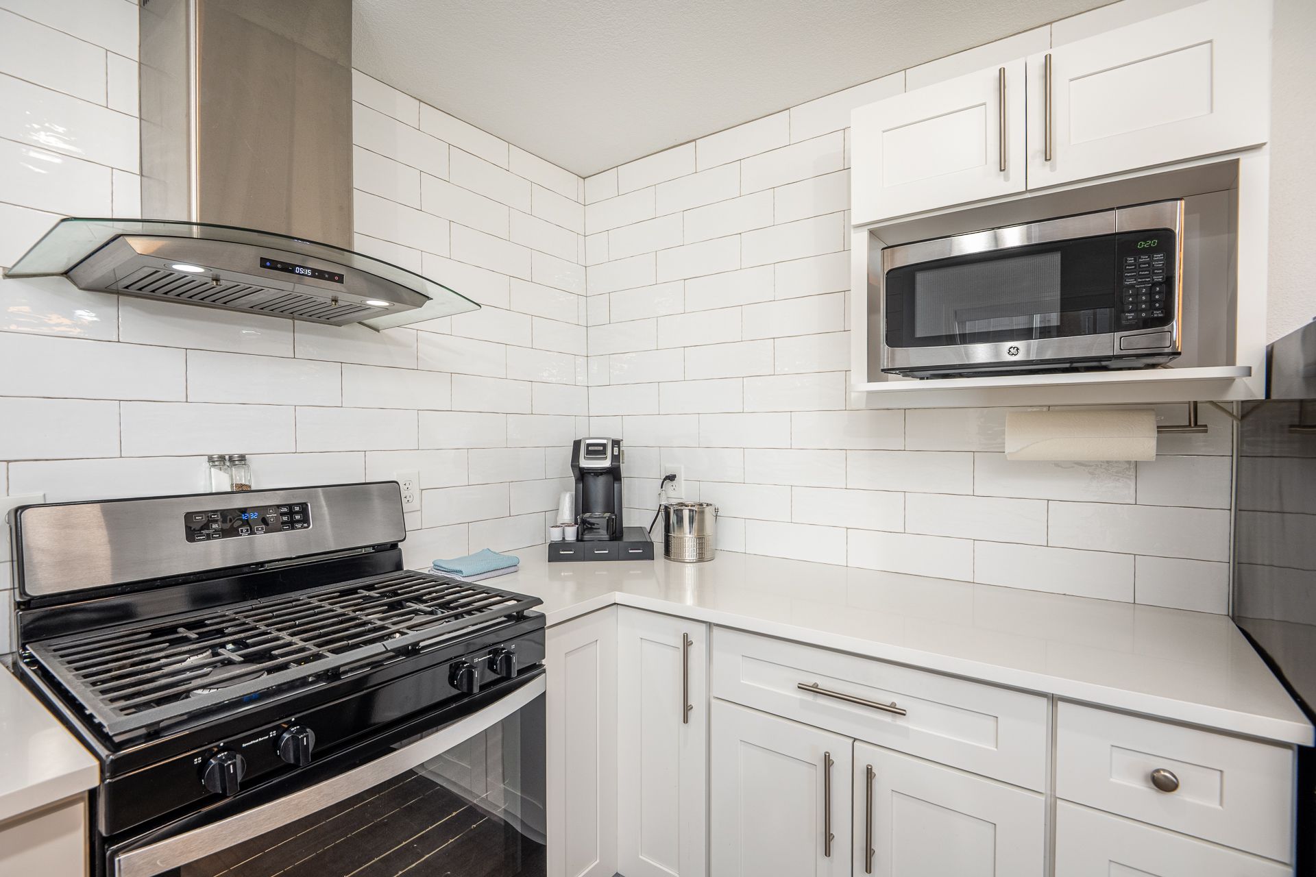 Modern kitchen featuring white cabinets, subway tile walls, stainless steel stove, range hood, and built-in microwave.