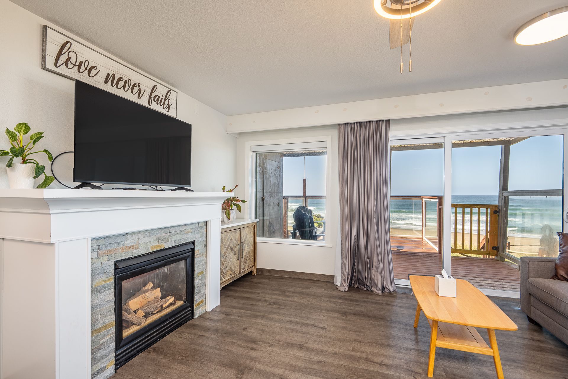 A living room with a fireplace, television, wooden coffee table, and a sliding glass door looking out to the ocean.