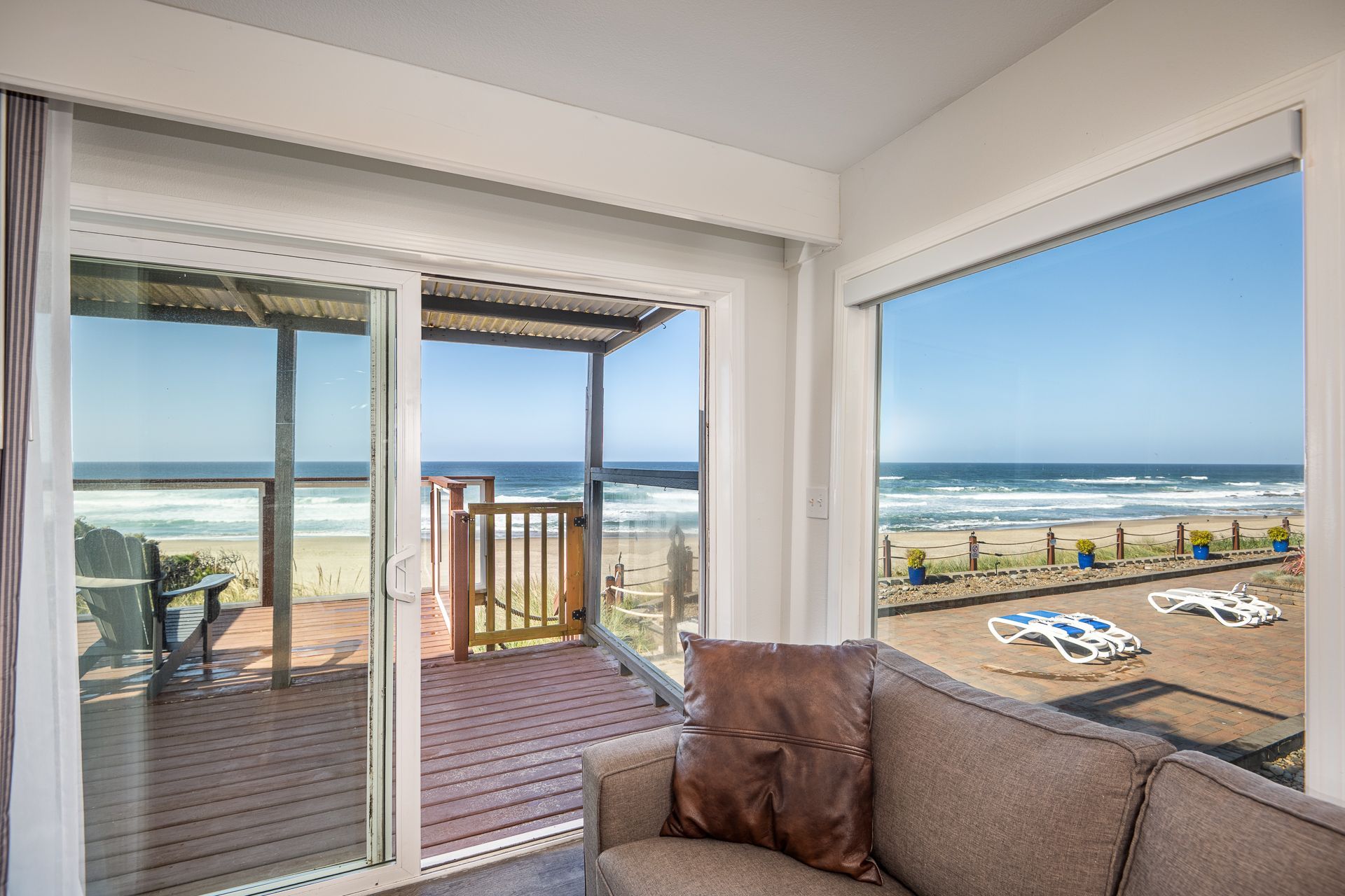 A brown couch faces a view of the beach and ocean through large sliding glass doors and a picture window.