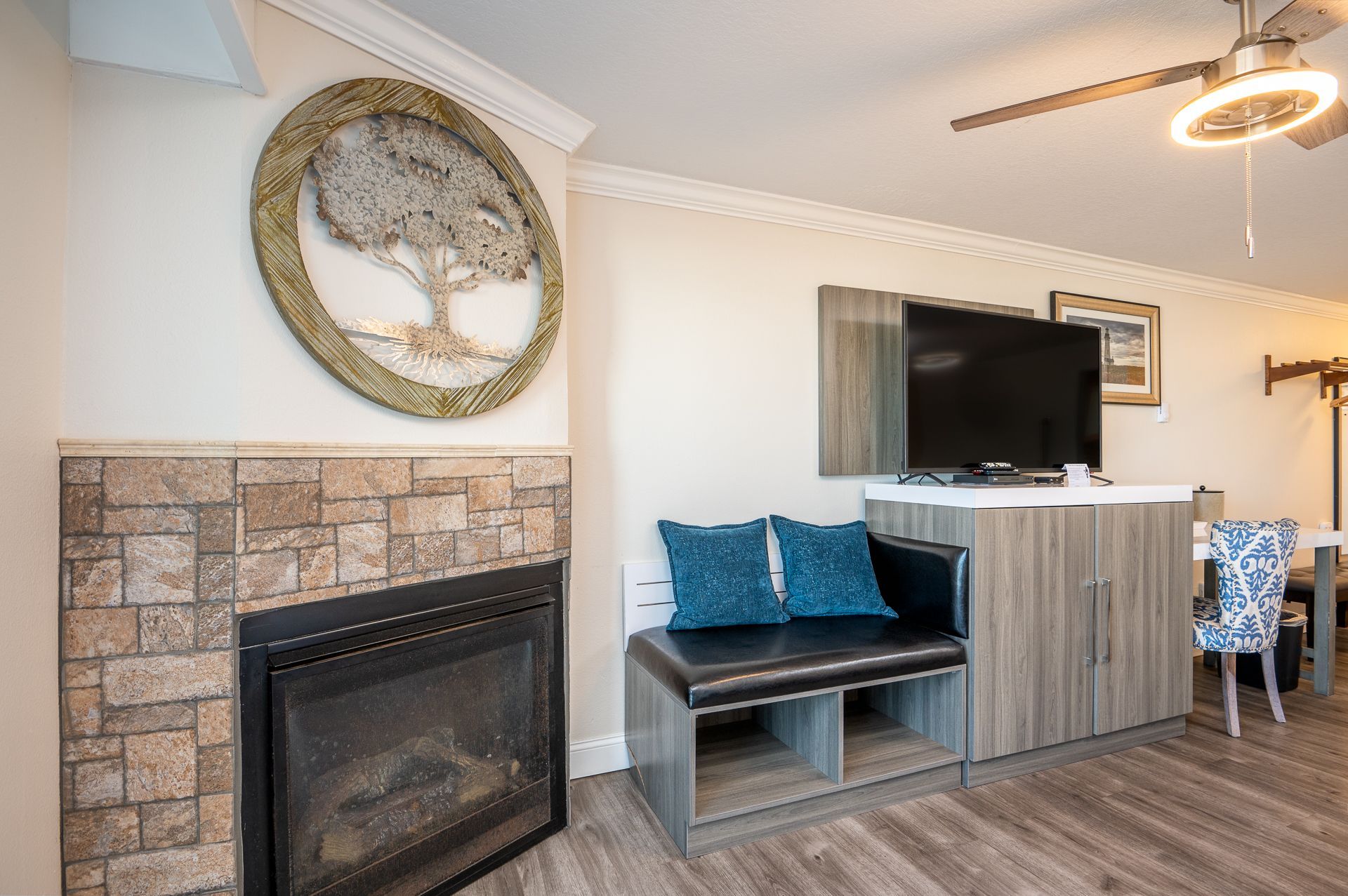 A stone fireplace with round tree art above, next to a black bench and a TV stand with a television in a modern room.
