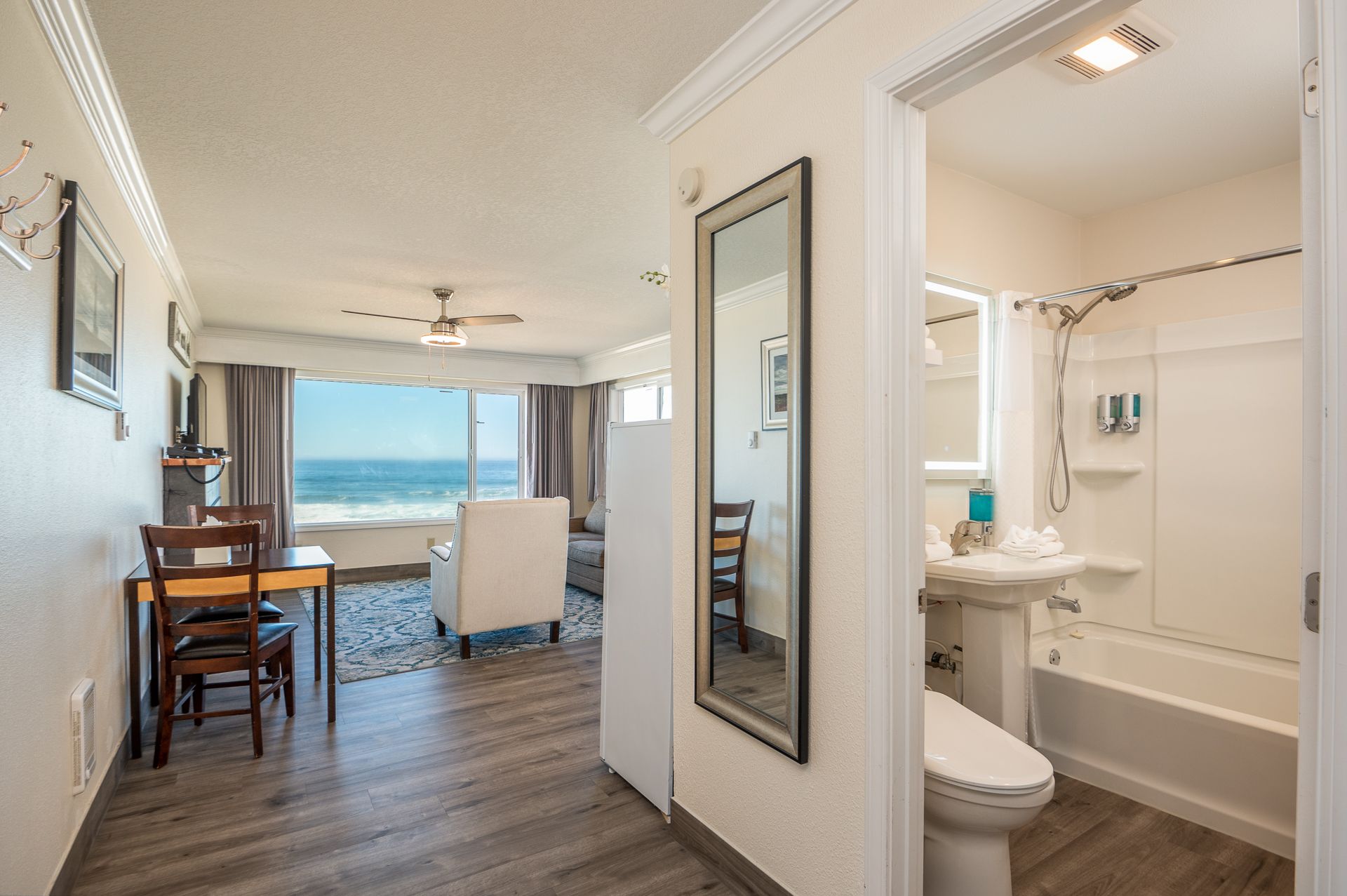 A hotel room featuring a dining area, a living space with an ocean view, and an adjacent bathroom with a shower-tub combo.