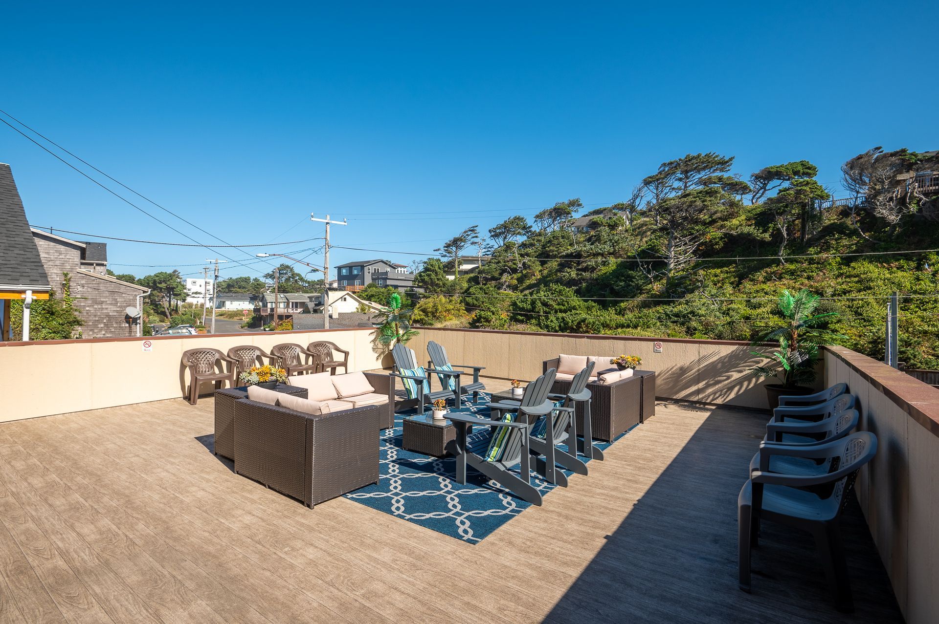 A spacious rooftop deck under a bright blue sky, featuring outdoor lounge furniture and seating on a patterned rug.