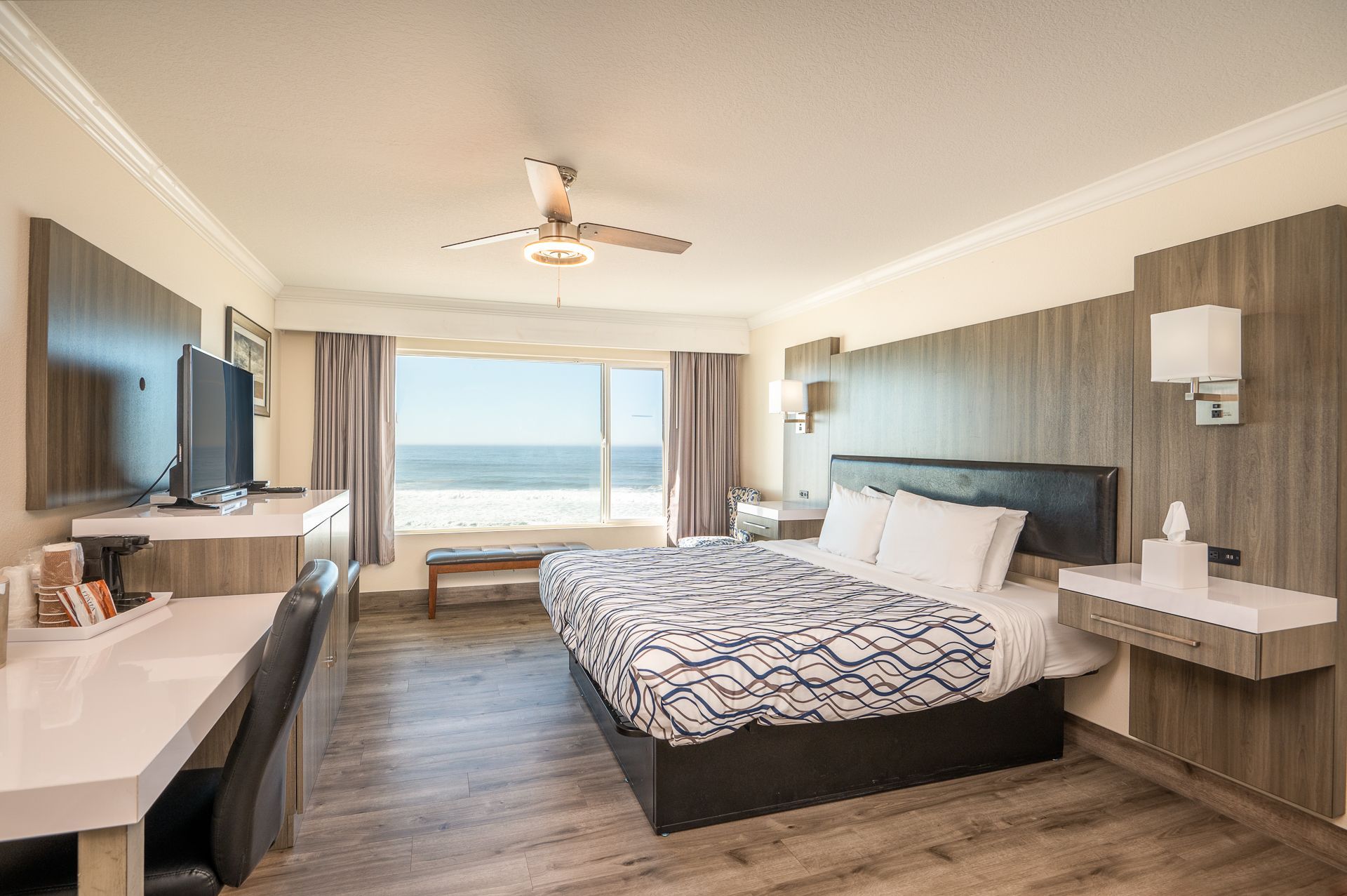 Hotel room with ocean view: bed, desk, sofa, and window with beach and water visible.