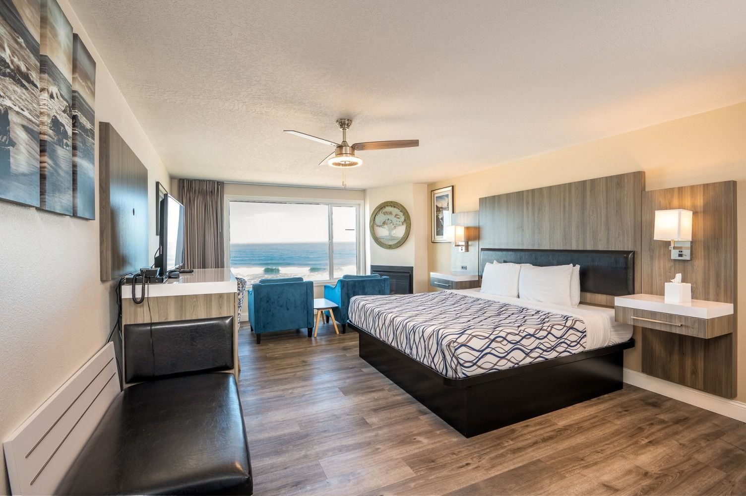 Hotel room with ocean view, king bed, seating area, mounted TV, and wooden floors.