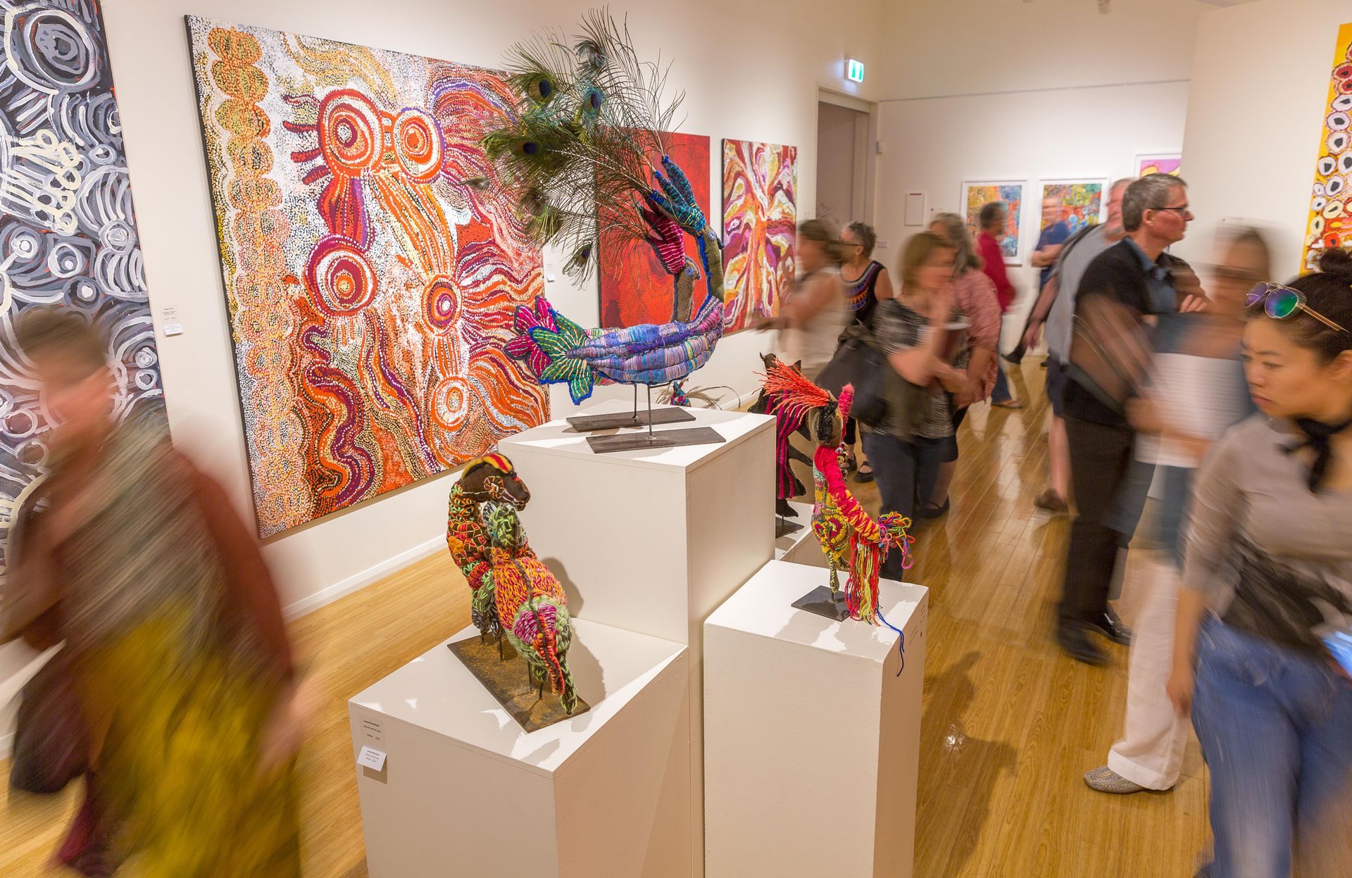 a group of people are standing in a museum looking at paintings and sculptures .