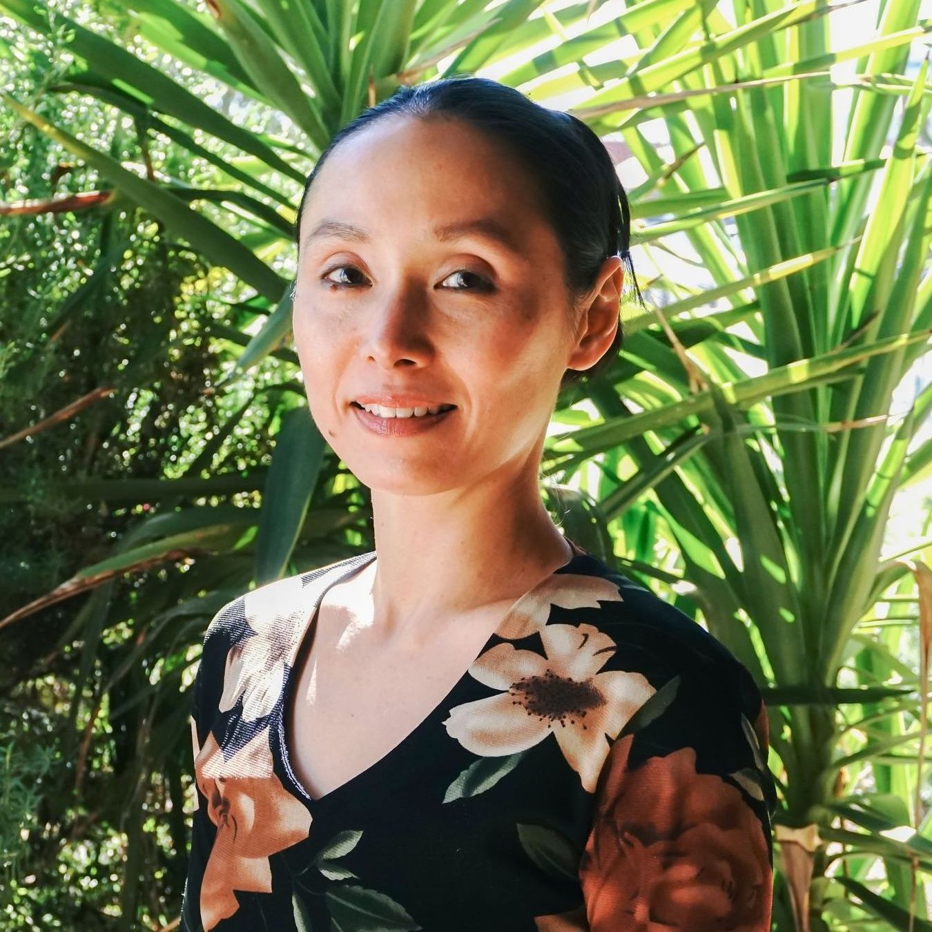 a woman in a floral dress is standing in front of a palm tree .
