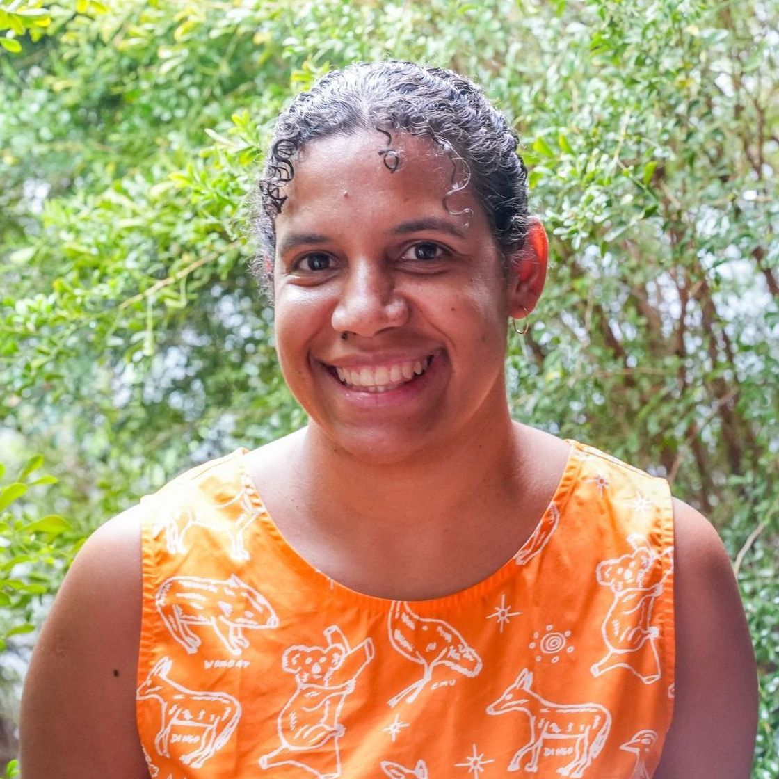 a woman in an orange tank top is smiling in front of trees .