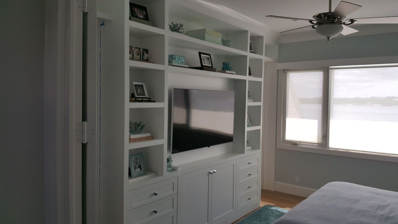 A bedroom with a large entertainment center with a flat screen tv and a ceiling fan.