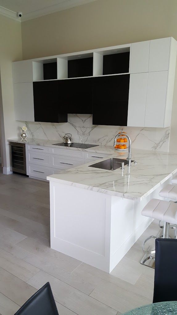 A kitchen with white cabinets , marble counter tops , a sink and a refrigerator.