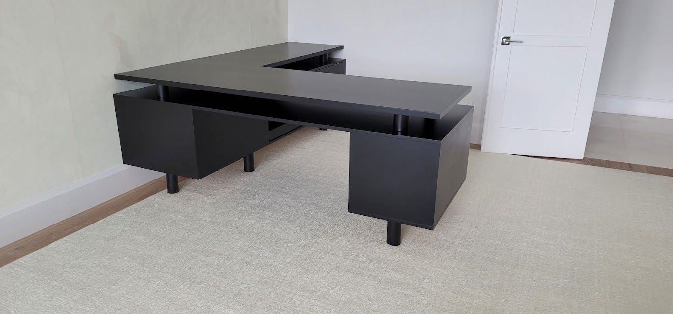 A black desk is sitting on top of a white carpet in a room.