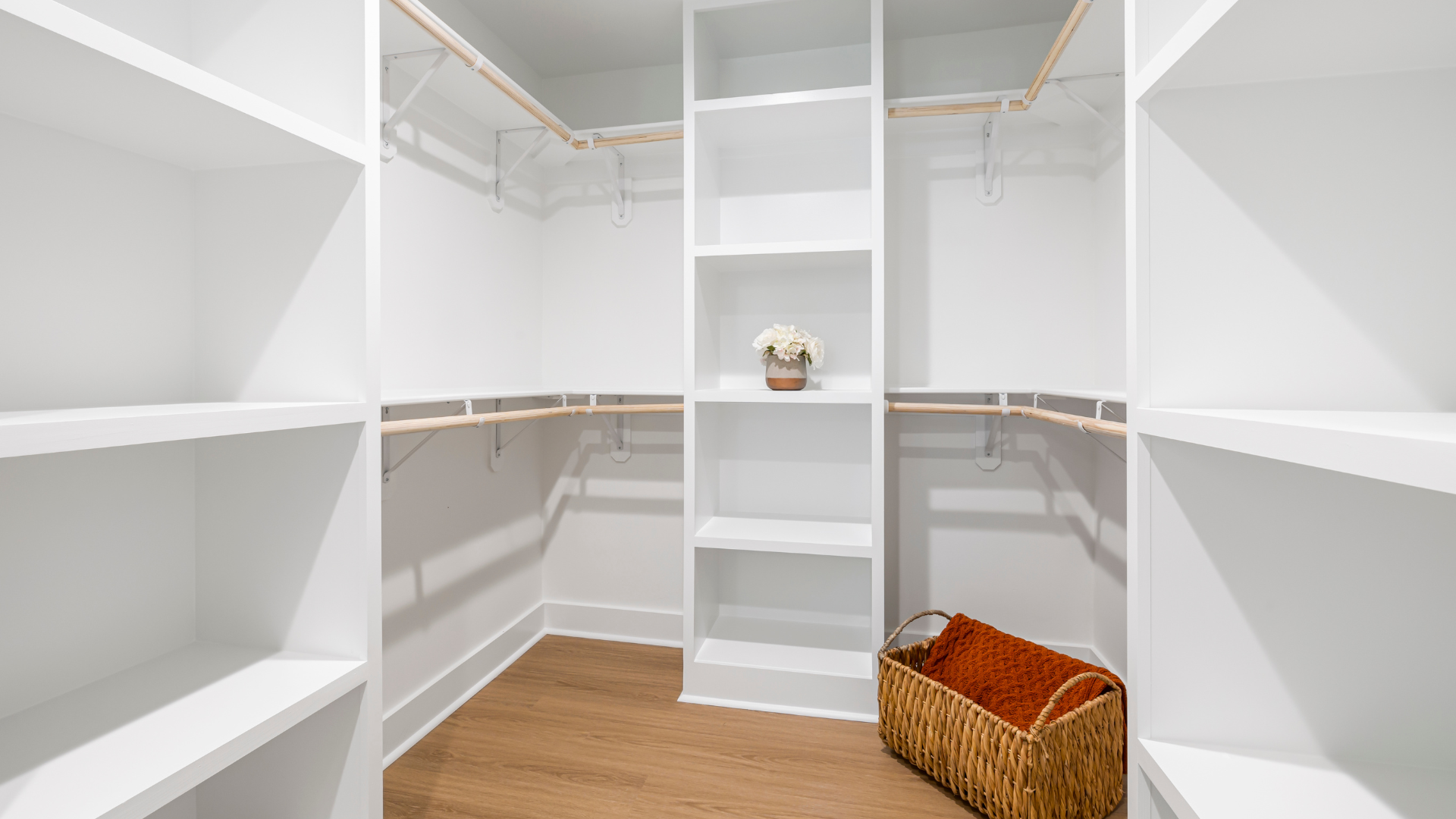An empty walk in closet with white shelves and a basket.