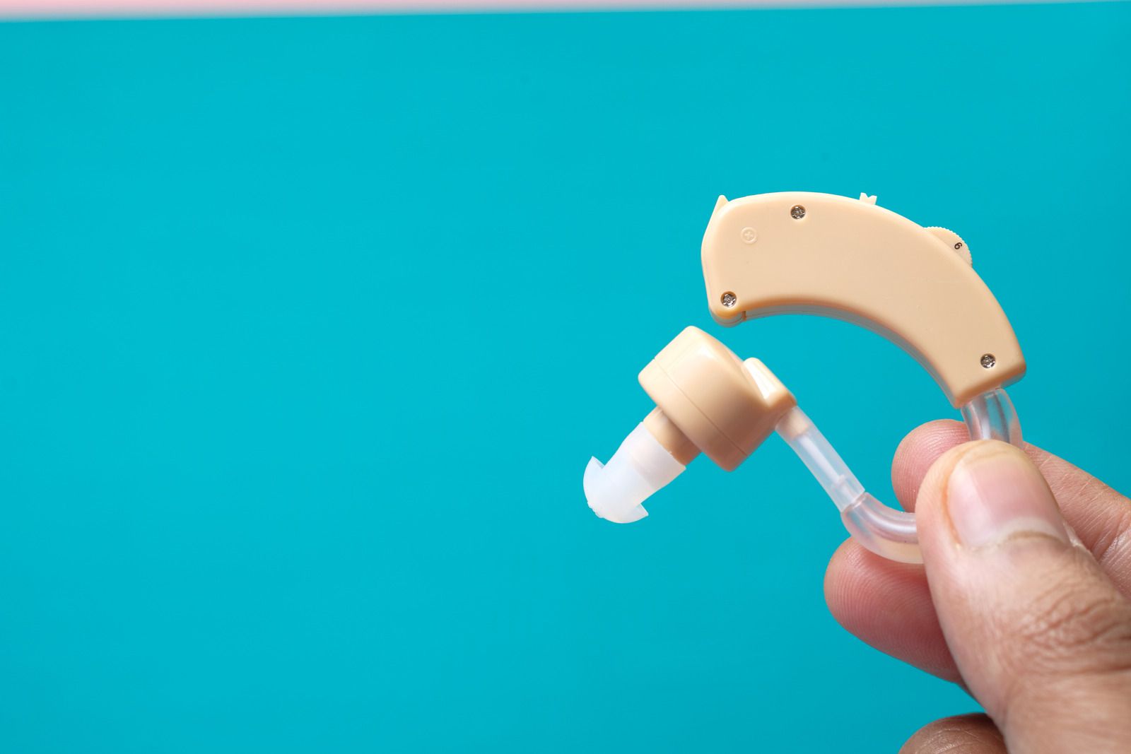 Hand holding a beige hearing aid against a turquoise background.