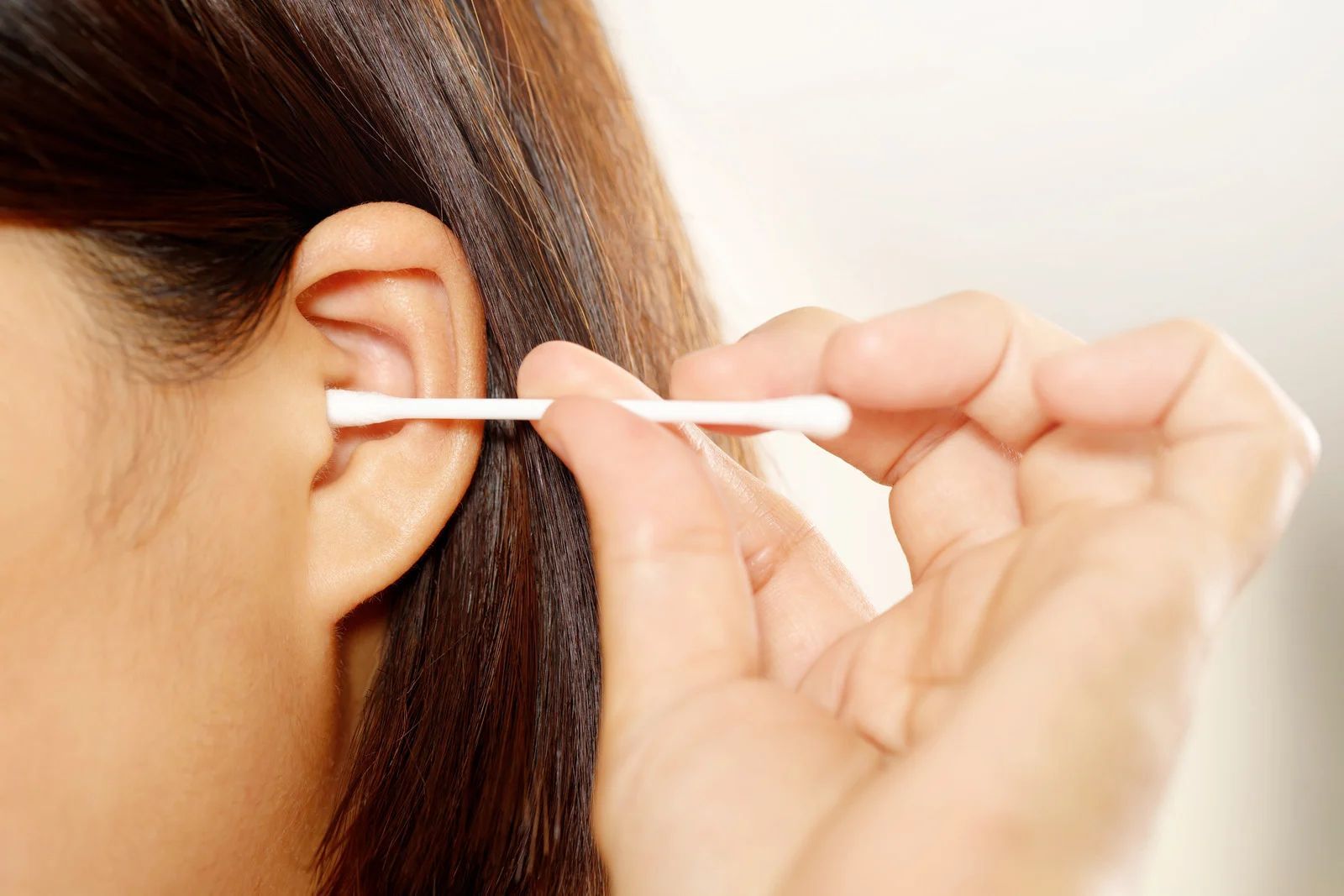 Woman cleaning her ear with a cotton swab.