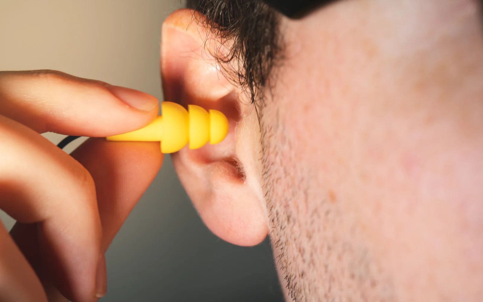 Person inserting yellow earplug into their ear.