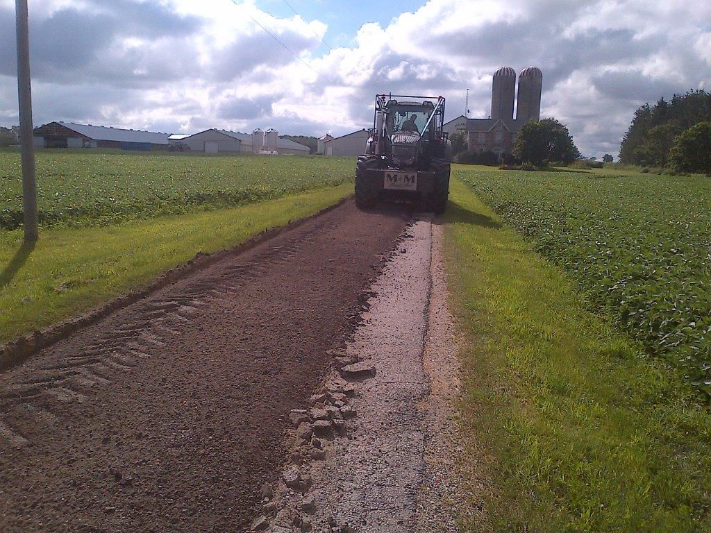 A tractor on a dirt road with a farm in the background