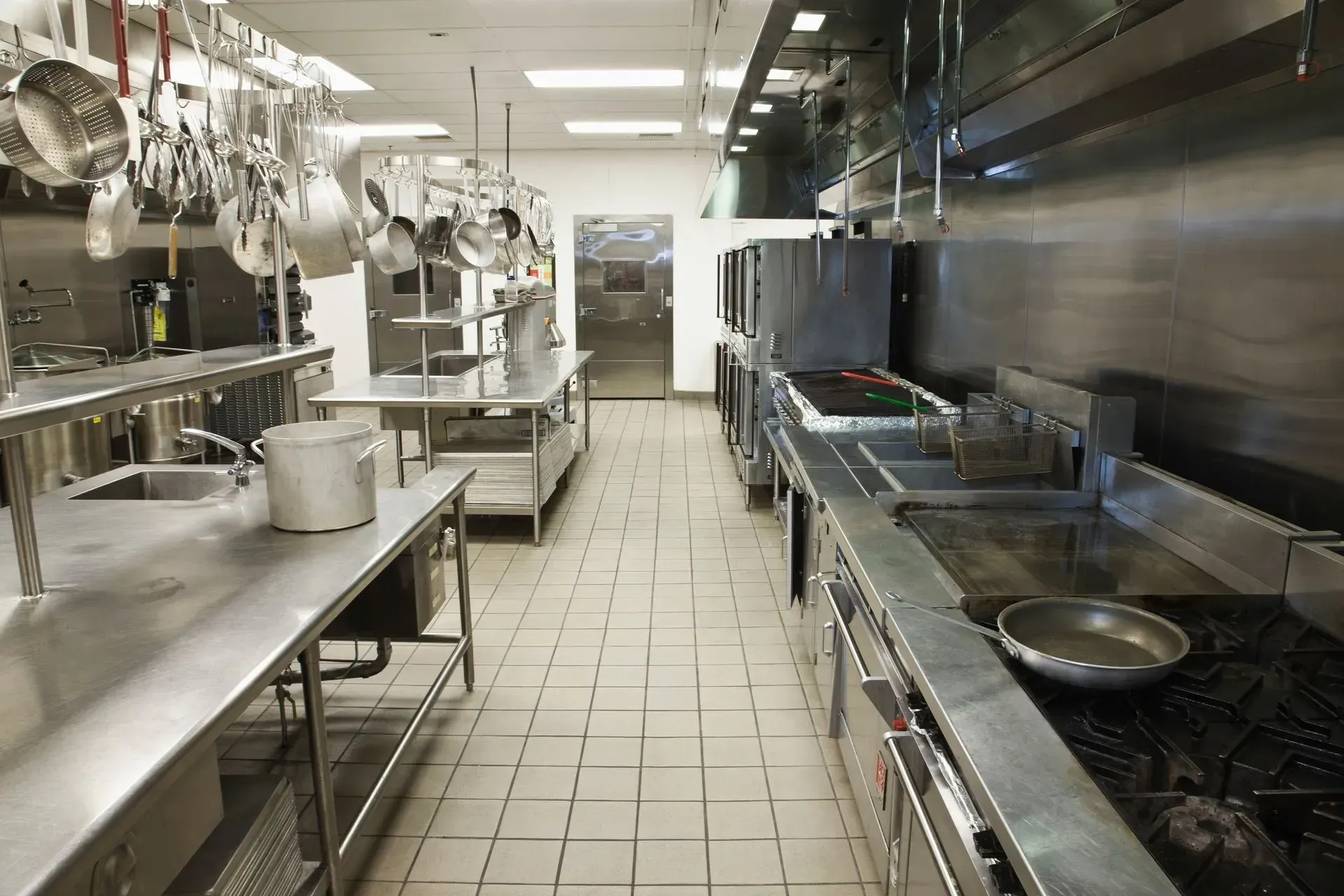 An empty kitchen with stainless steel appliances and pots and pans hanging from the ceiling