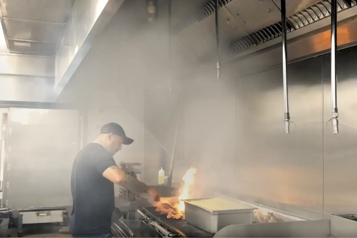 A man is cooking food on a grill in a kitchen.