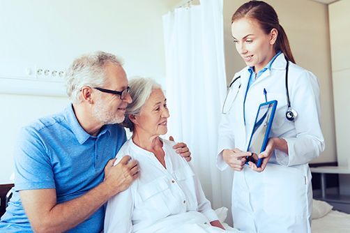 A healthcare provider in a white lab coat shows information on a tablet to two people sitting in a medical room.