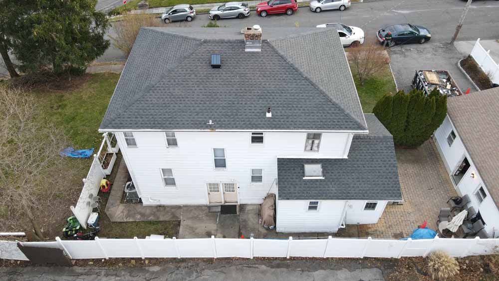 An aerial view of a white house with a black roof and a white fence.