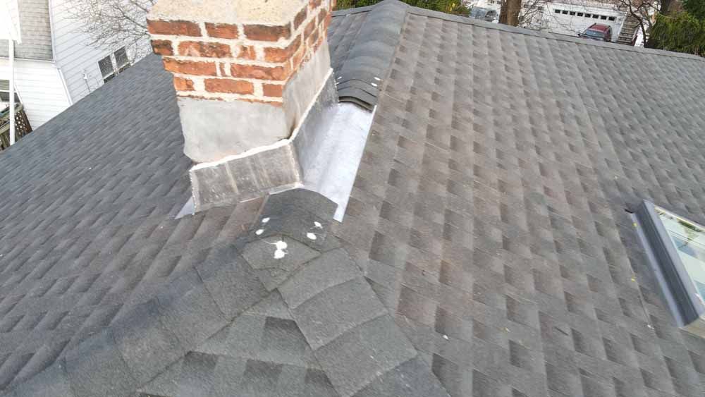 A roof with a chimney and a skylight on it.