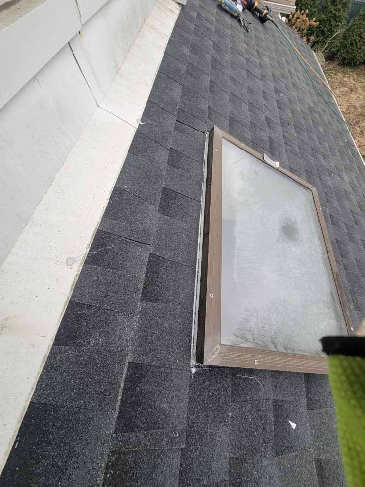 A roof with shingles and a skylight on it.