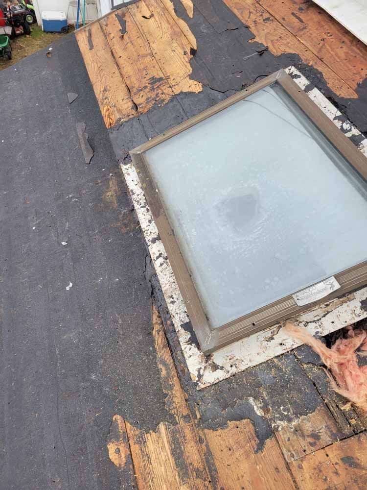 A skylight is sitting on top of a roof that is being repaired.