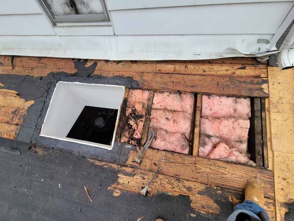 A person is standing next to a hole in the roof of a house.