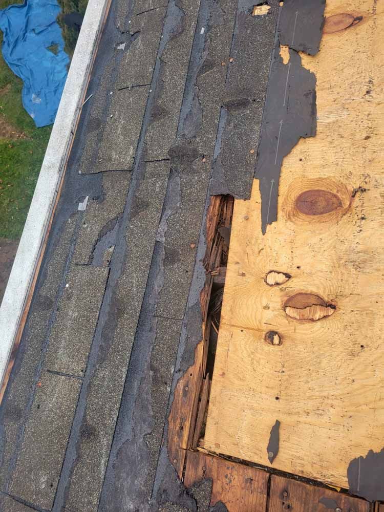 A close up of a roof with shingles missing and a hole in it.