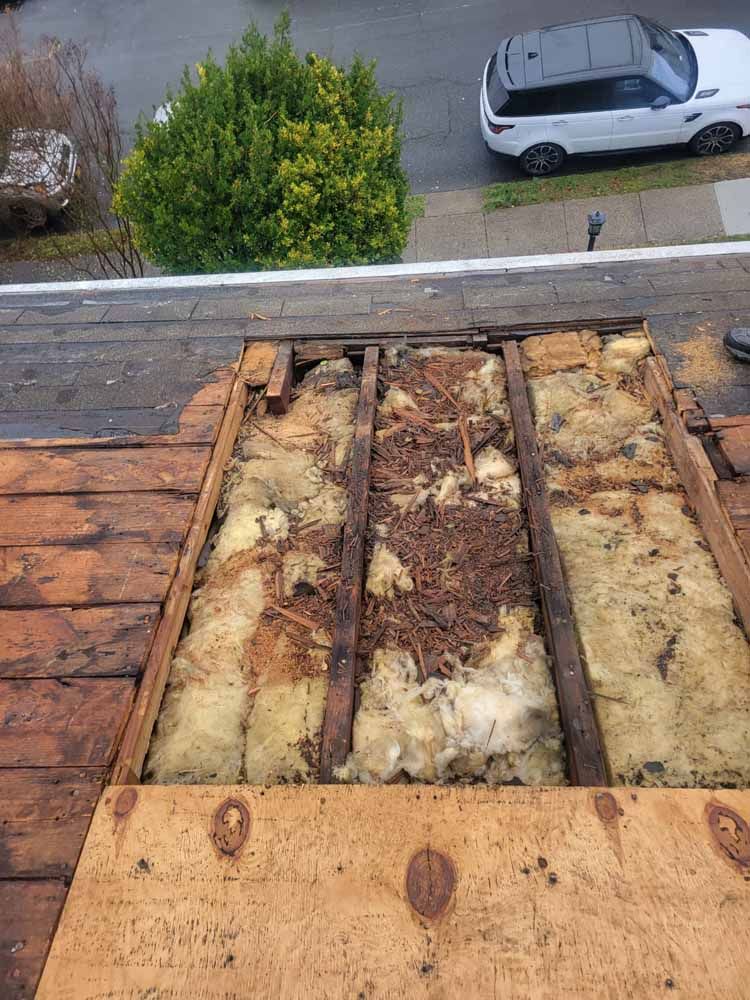 A car is parked on the side of the road next to a wooden roof.