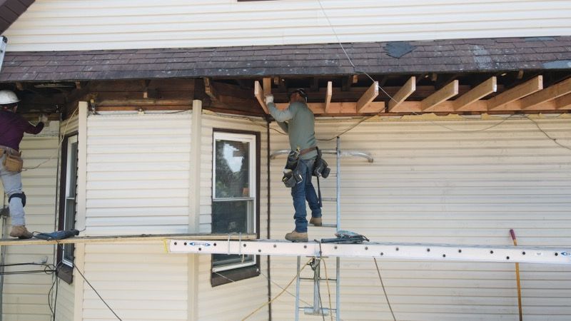 Two men are working on the side of a house.