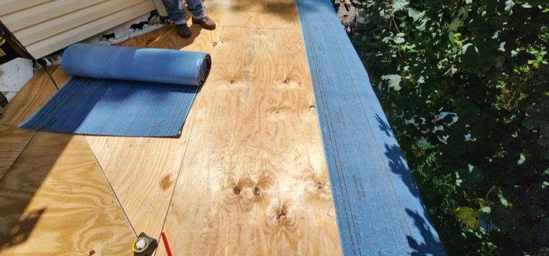 A person is laying a roll of blue tape on a wooden floor.