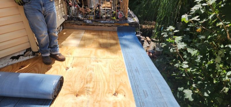 A man is standing on a wooden deck next to a roll of blue tarp.