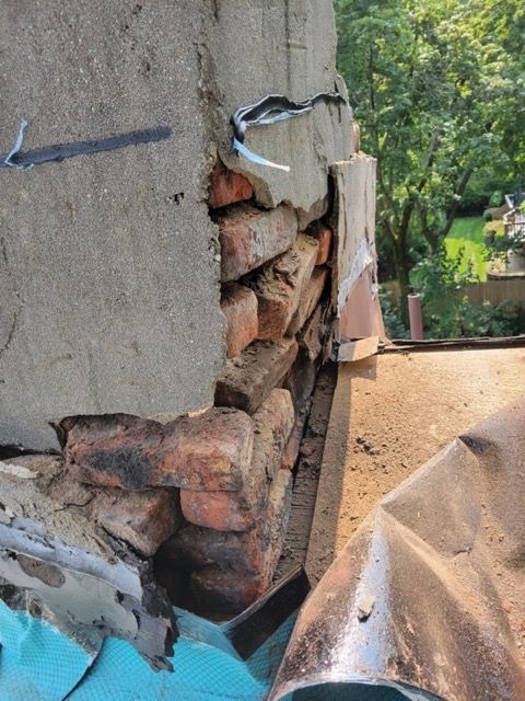 A brick wall with a hole in it and a blue tarp on the ground