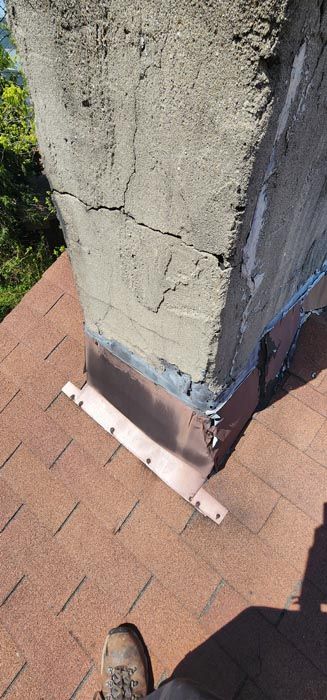 A person is standing on a roof next to a chimney.