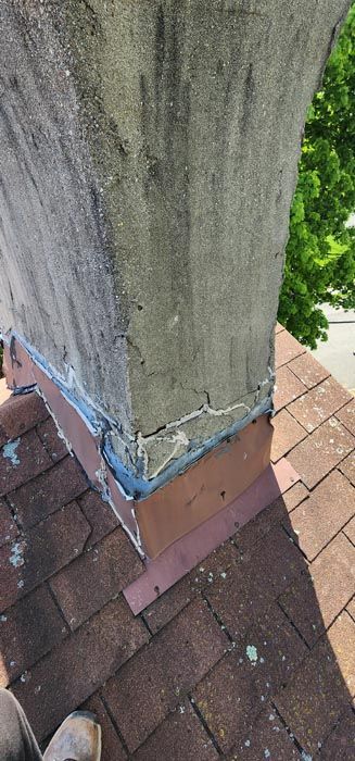 A person is standing on top of a brick roof next to a chimney.