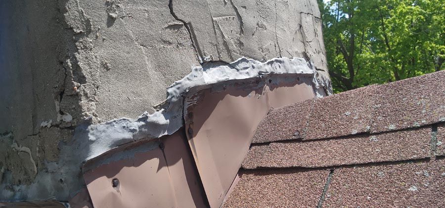 A close up of a roof with a chimney in the background.