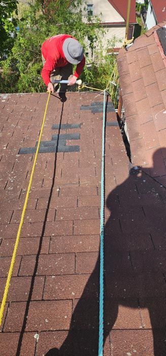 A man is measuring a roof with a tape measure.