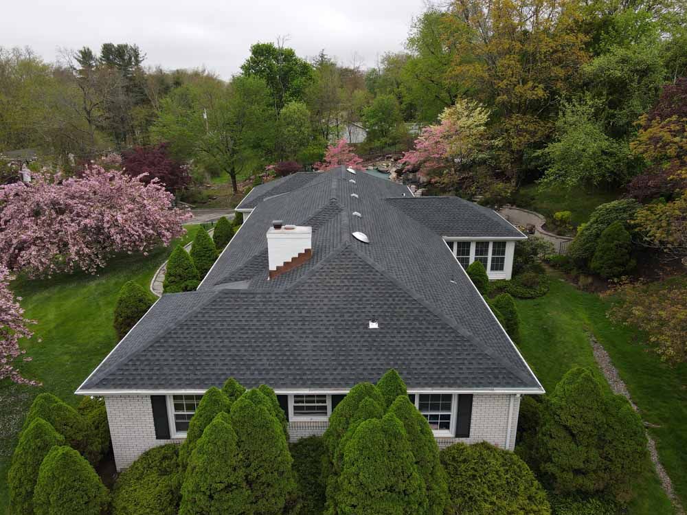 An aerial view of a house with a black roof surrounded by trees and bushes.