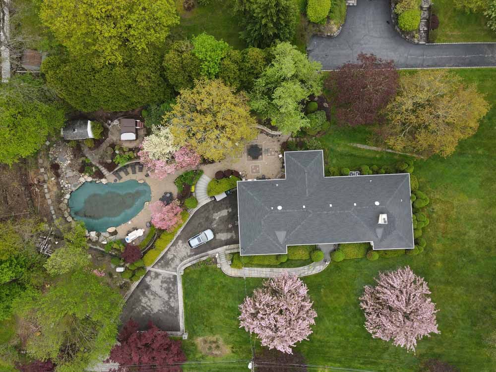 An aerial view of a house with a pool in the backyard surrounded by trees.