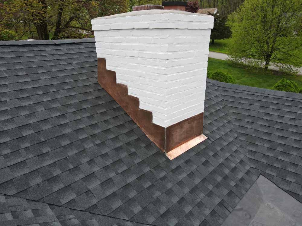 A chimney on top of a roof with a black shingle.