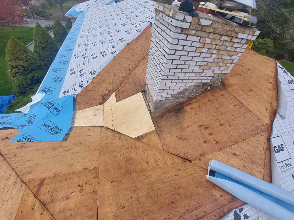 A roof with a chimney on top of it is being repaired.